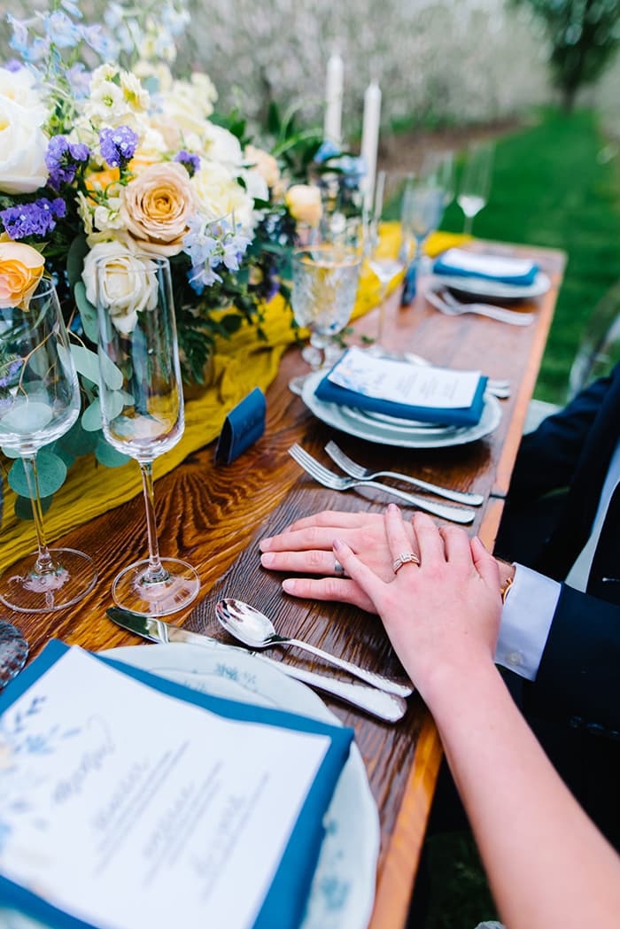 A bride and groom hold hands by a lavishly decorated wedding head table.